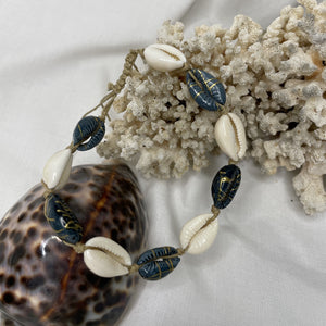 bracelet de cheville réglable en coquillage cauri balnc et gris foncé avec détails dorés. taille réglable avec noeud macramé